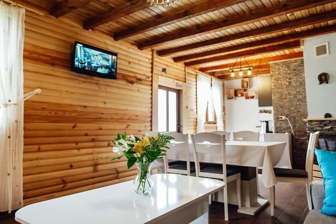 A wooden interior with a dining area, a television mounted on the wall, and a stone wall.