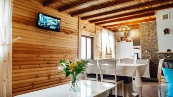 A wooden interior with a dining area, a television mounted on the wall, and a stone wall.