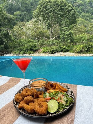 Una taula de menjador amb un plat de menjar, una beguda i vista a una piscina.