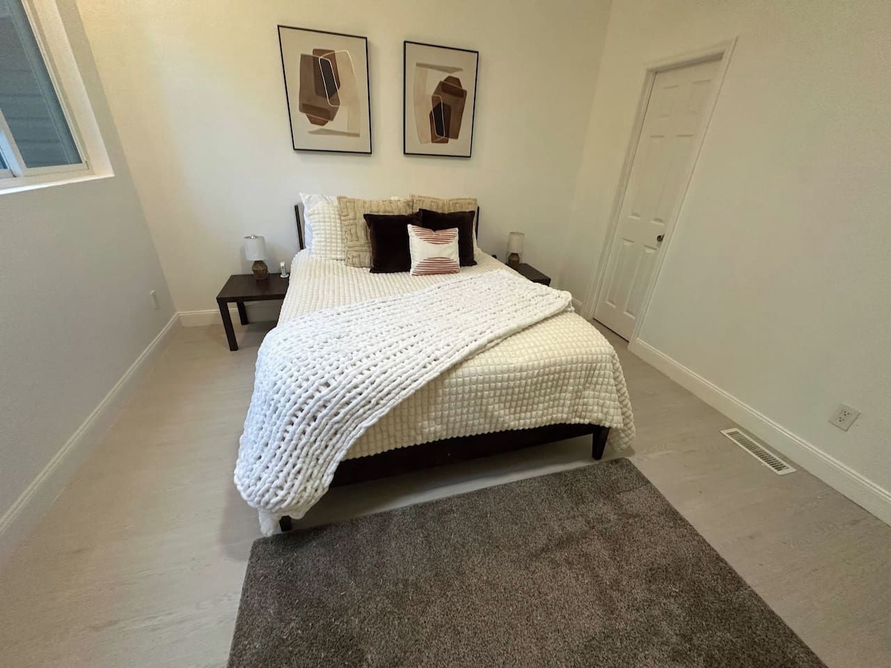 A bedroom with a bed, a nightstand, a bedside table, a wall-mounted light, and a door.