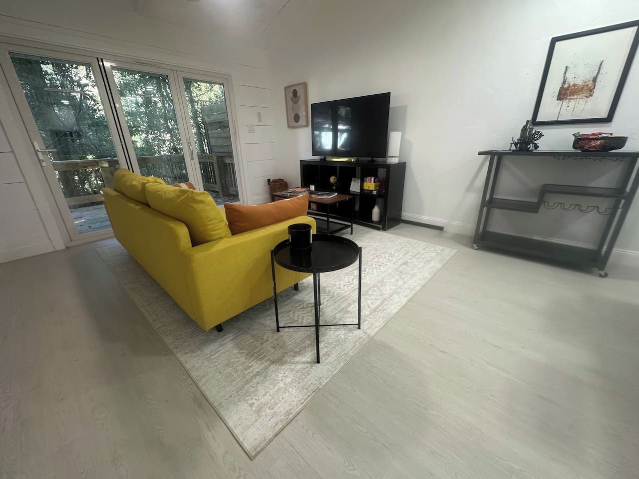 Un salon avec un canapé jaune, une table basse noire, un téléviseur à écran plat et une cheminée.