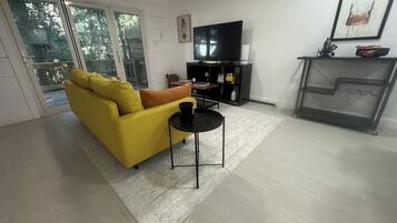 Un salon avec un canapé jaune, une table basse noire, un téléviseur à écran plat et une cheminée.