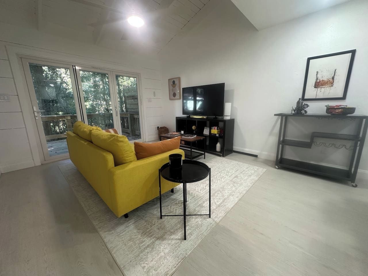 Een woonkamer met een gele bank, een zwarte salontafel, een flatscreen televisie en een boekenplank.