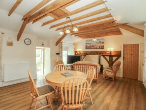 A dining area with wooden chairs and a round table, a fireplace, and a television. - BRYN EITHIN, family friendly, country holiday cottage in Carmel (Caernarfon)