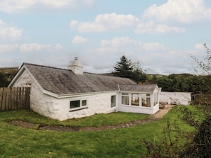 A white house with a sloped roof and a conservatory. - BRYN EITHIN, family friendly, country holiday cottage in Carmel (Caernarfon)
