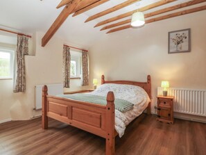A bedroom with a wooden bed, two bedside lamps, a radiator, and a window with curtains. - BRYN EITHIN, family friendly, country holiday cottage in Carmel (Caernarfon)
