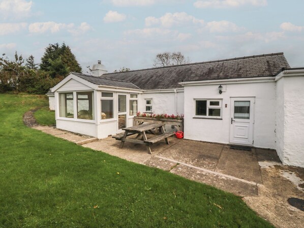 A white building with a conservatory, a patio with a table and chairs, and a small garden area. - BRYN EITHIN, family friendly, country holiday cottage in Carmel (Caernarfon)