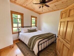 Una camera da letto con un letto, due finestre, una ventola a soffitto e una porta in legno.