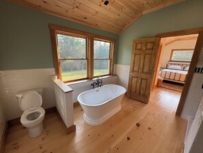 Un bagno con pavimento in legno, una vasca da bagno indipendente, un WC e una finestra vista esterna.