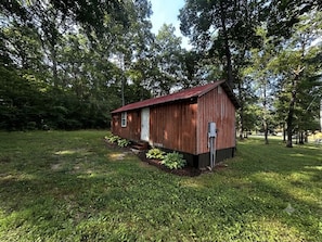 A wooden cabin with a red roof, surrounded by a grassy area and trees.