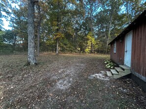 A cabin with a dirt path leading to a wooden door, surrounded by trees and a grassy area.