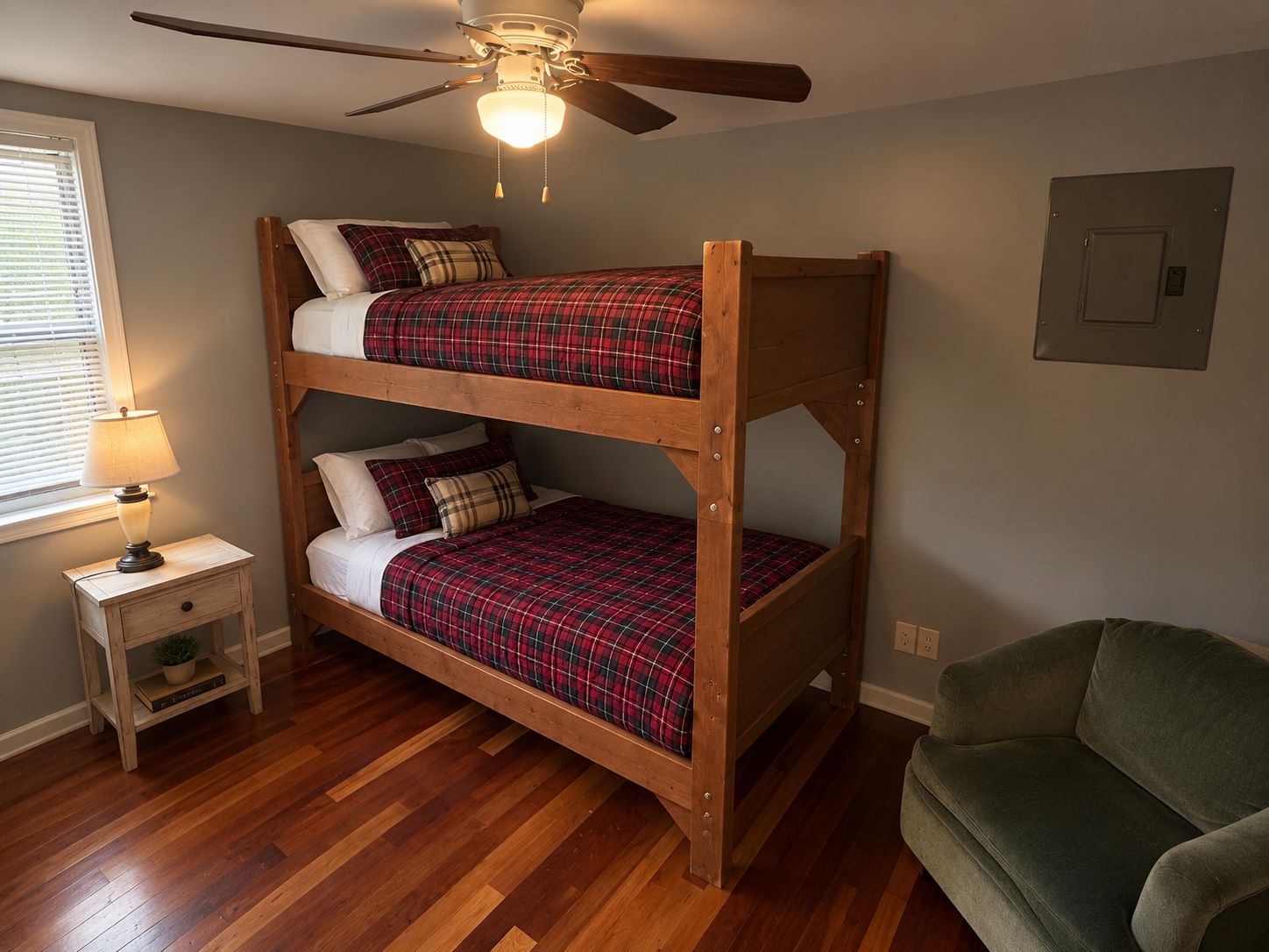 Ein Etagenbett mit Deckenventilator, ein Nachttisch mit Lampe und ein grüner Stuhl in einem Zimmer mit Holzböden.