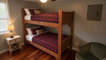 A bunk bed with a ceiling fan, a bedside table with a lamp, and a green chair in a room with wooden flooring.