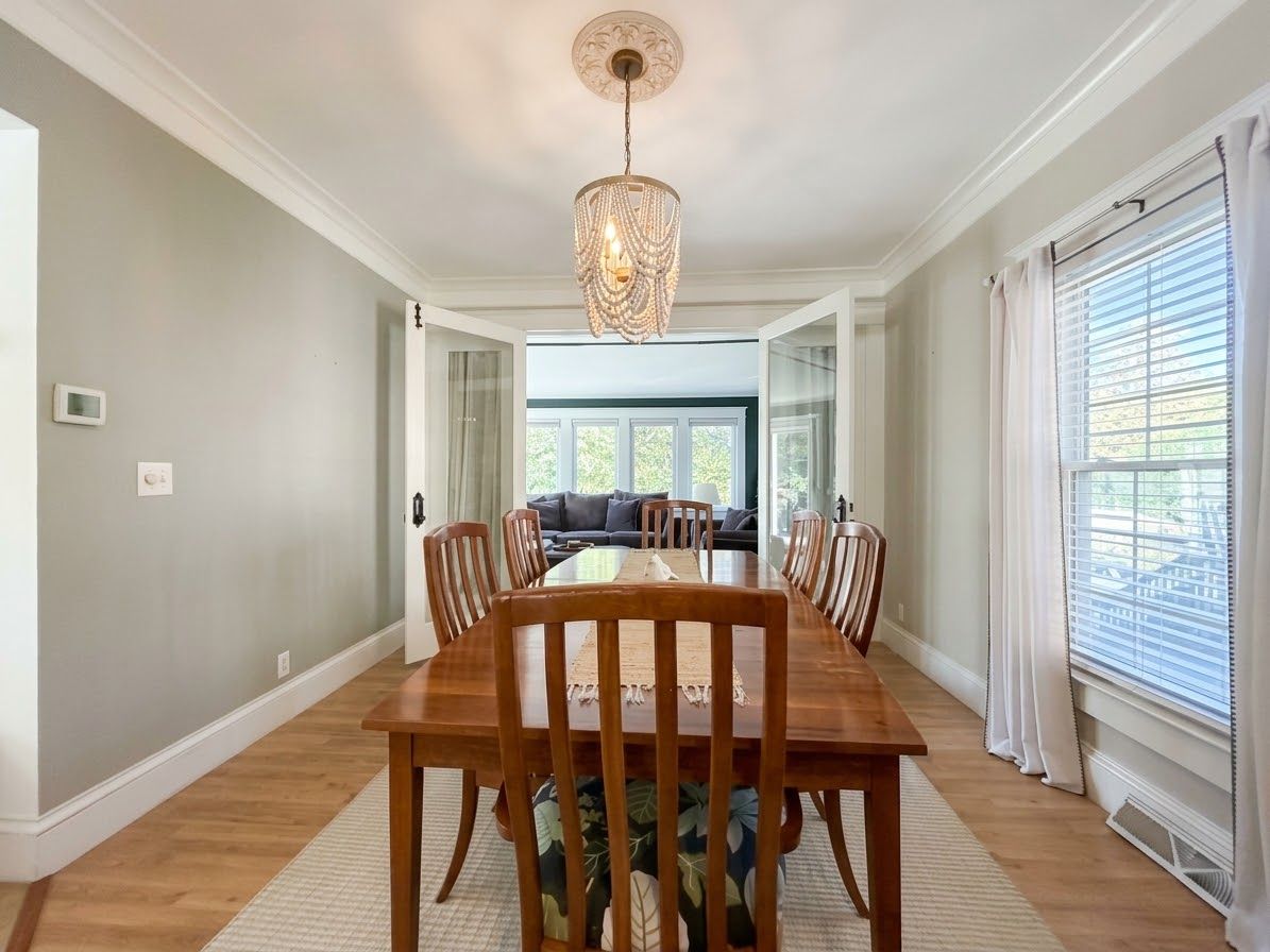 Une salle à manger avec une table et des chaises en bois, un lustre et une vue sur le salon.