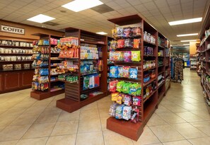 Een gangpad in een supermarkt met schappen vol snacks, drankjes en huishoudelijke producten.