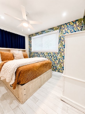 A bedroom with a bed, a ceiling fan, a window with blinds, and a wall with a floral pattern. - 1BR + Office Near DTO, Large Fenced Yard, Dogs Welcome (Orlando)