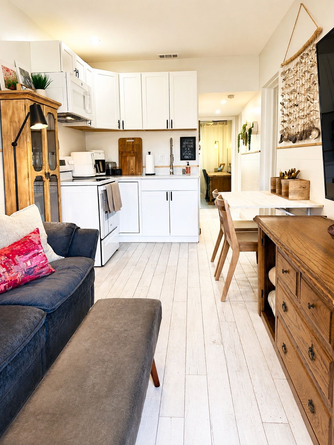 Un espace de vie compact comprenant un coin cuisine, un coin repas et un espace détente avec un canapé et un pouf.