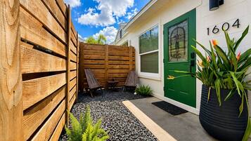 A residential property with a green door marked '1604,' a wooden fence, outdoor seating, and a potted plant.