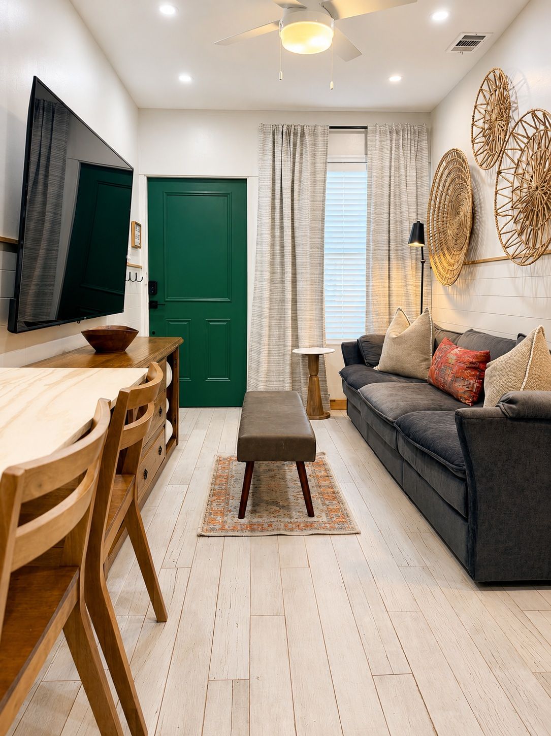 A modern living room with a dining area, a green door, and a large window with curtains.