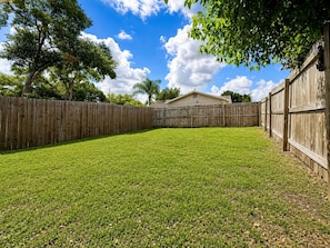 A fenced backyard with a grassy lawn, a wooden fence, and a house in the background. - 1BR + Office Near DTO, Large Fenced Yard, Dogs Welcome (Orlando)