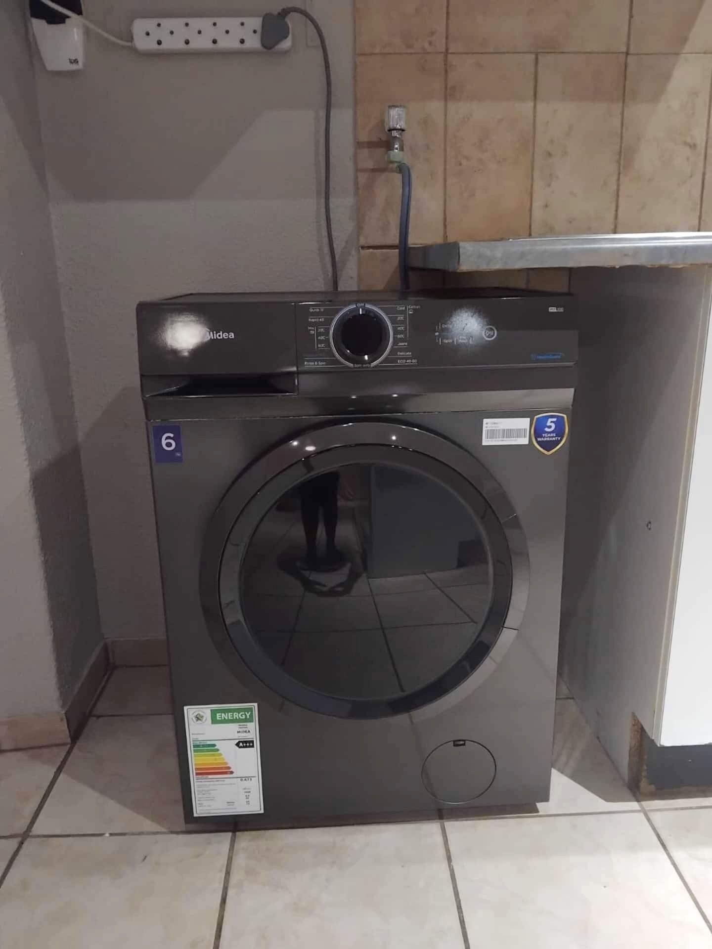 A front-loading washing machine with a control panel, a water inlet hose, and a label indicating energy efficiency.