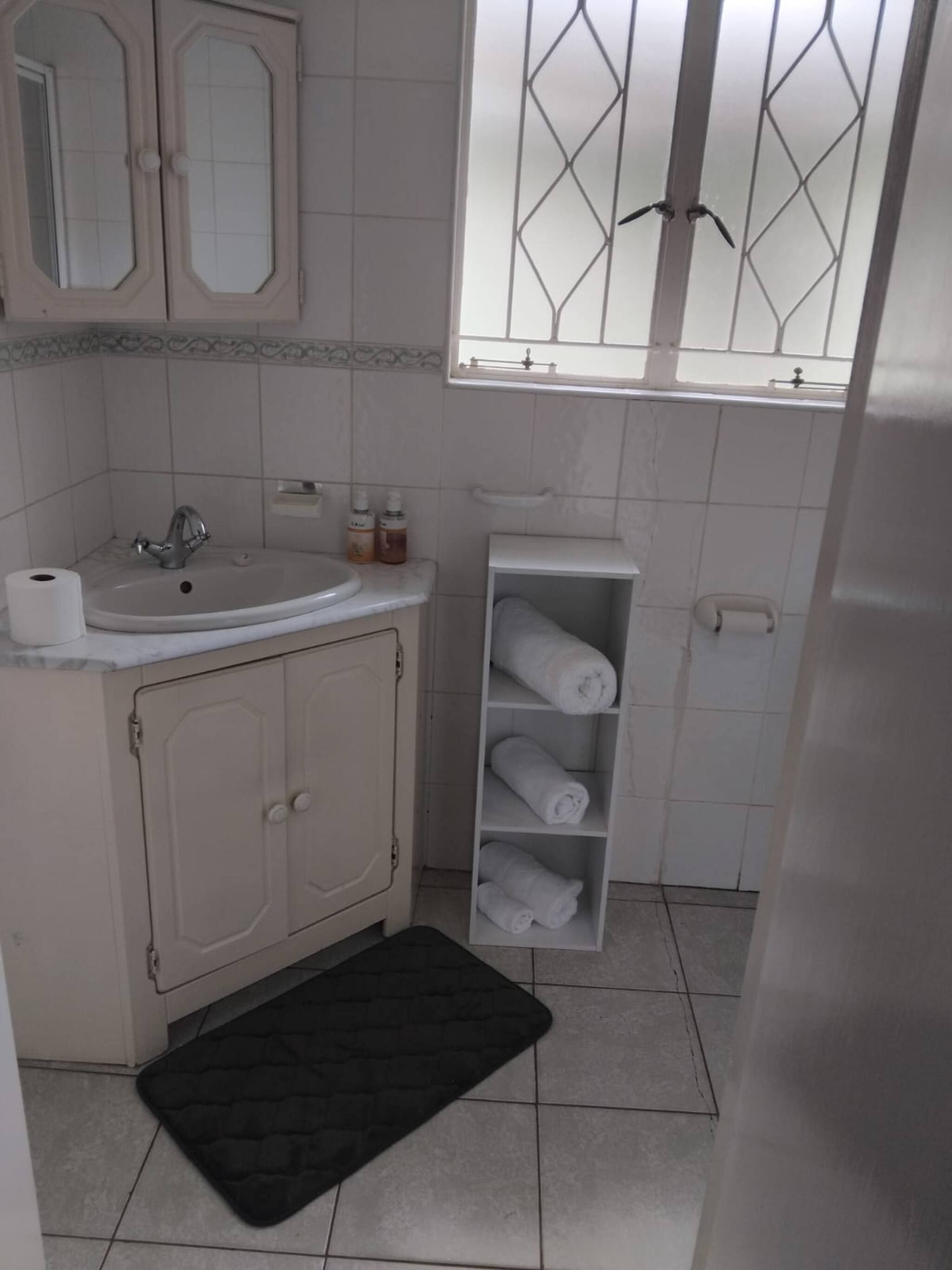 Un baño con lavamanos, espejo, toallero y ventana con reja de metal.