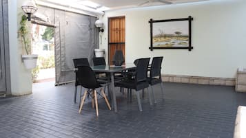 Een terras buiten met een tafel, stoelen, een plafondventilator en een gekaderd schilderij aan de muur.