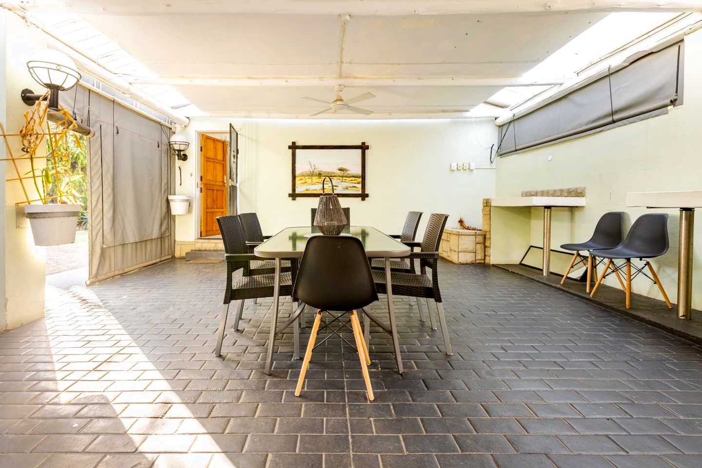 Un patio cubierto con mesa y sillas, un ventilador de techo y vistas al exterior.