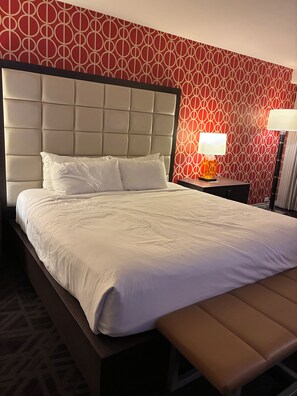 Une chambre d’hôtel avec un grand lit, une tête de lit, une table de chevet avec une lampe et un mur décoré d’un motif.