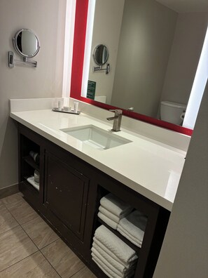 Un baño con un lavamanos blanco, dos espejos y un perchero para toallas.