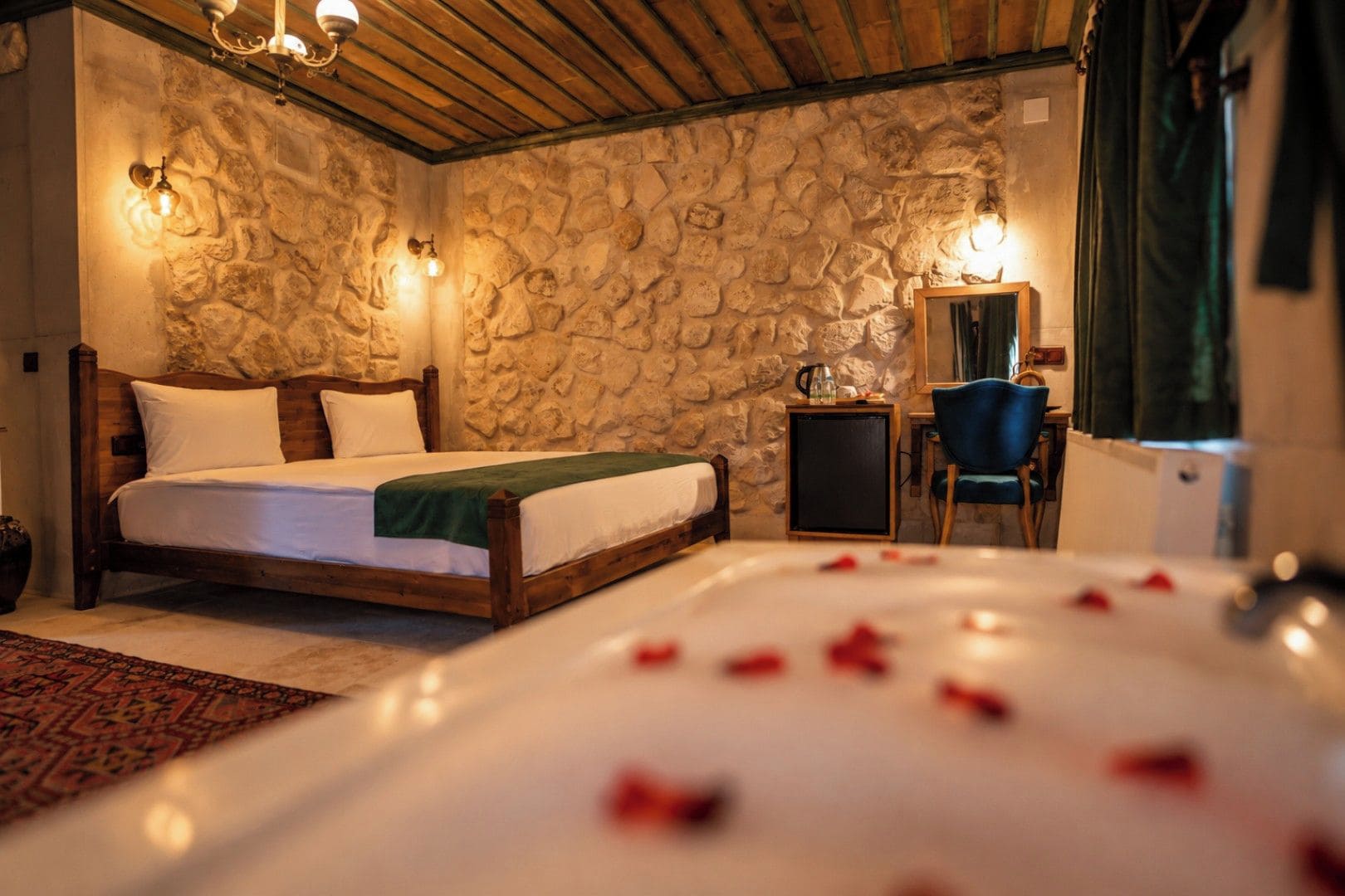 Un dormitorio con pared de piedra, una cama con ropa de cama blanca, una mesita de noche, una silla y un espejo.