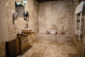 A bathroom with a marble floor, a wooden vanity with a bowl sink, a towel rack, and a shower area with a bathtub and two white basins. - Vista Rosa Cappadocia (Çavuşin)