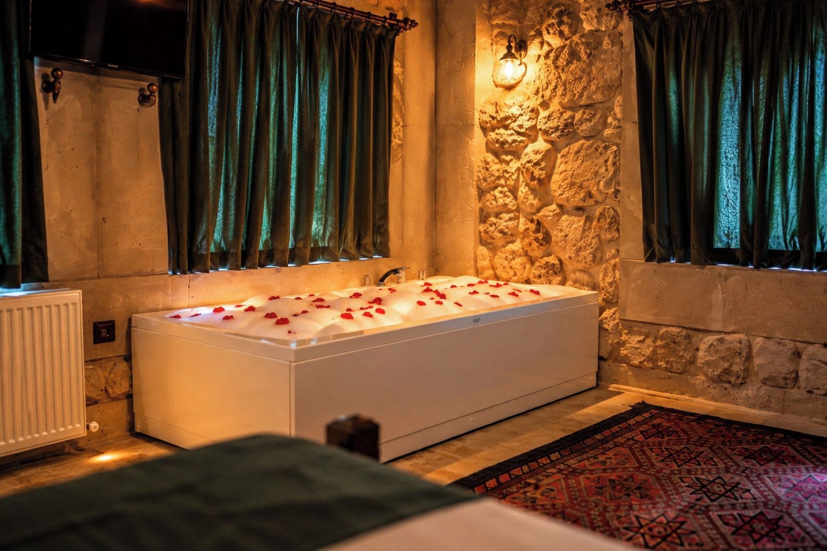Un baño moderno con una bañera grande, paredes de piedra y cortinas verdes.