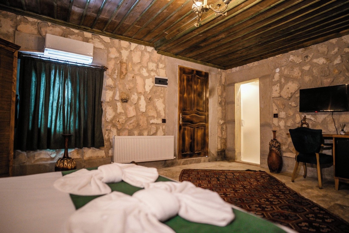 A room with a bed, a radiator, a stone wall, a wooden door, a television, and a chair.