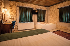 A bedroom with a stone wall, a bed, a wooden desk, a radiator, and a bathtub. - Vista Rosa Cappadocia (Çavuşin)