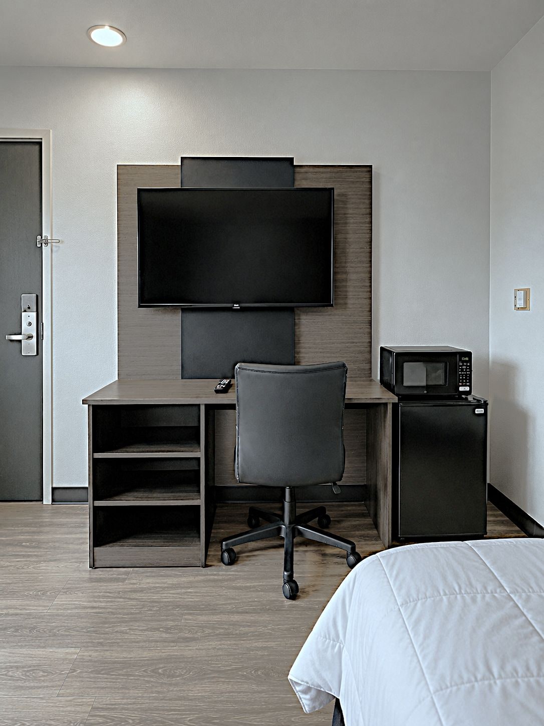 Quarto de hotel com cama, escrivaninha, cadeira, televisão e micro-ondas.