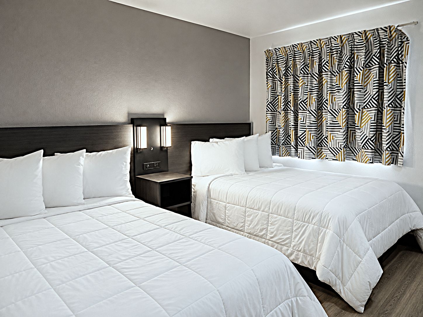 Une chambre d’hôtel avec deux lits, une table de chevet avec une horloge et des rideaux à motifs.