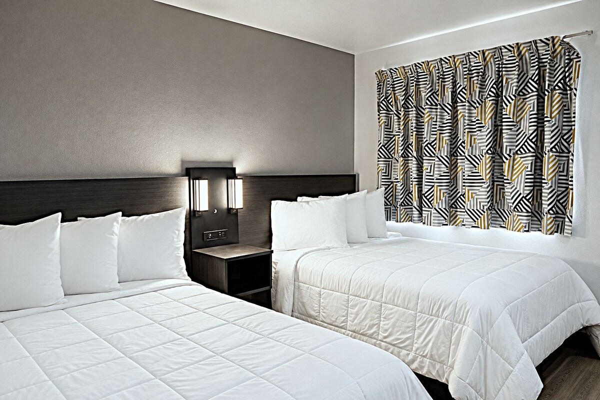 Une chambre d’hôtel avec deux lits, une table de chevet avec une horloge et des rideaux à motifs.
