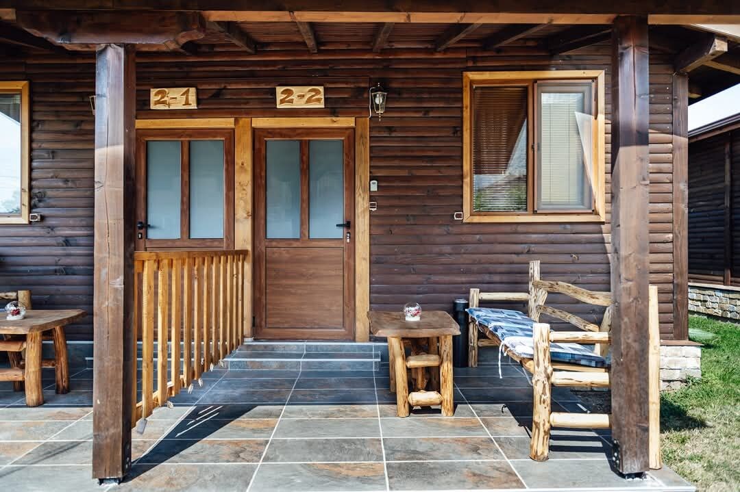 Eine Holzhütte mit zwei Türen, auf denen '2-1' und '2-2' stehen, einem kleinen Tisch und einer Bank vor der Tür.