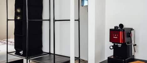 A room with a bunk bed, a red wall clock, a coffee machine, and a trash bin.