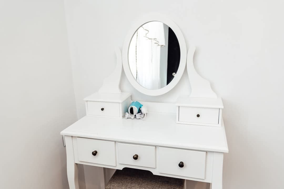 A white vanity with a mirror, three drawers, and a small blue object on the counter.