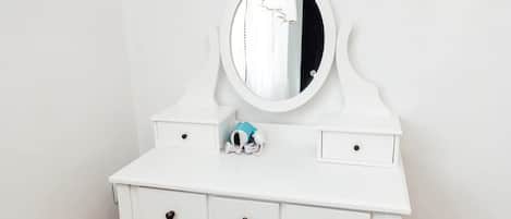 A white vanity with a mirror, three drawers, and a small blue object on the counter.