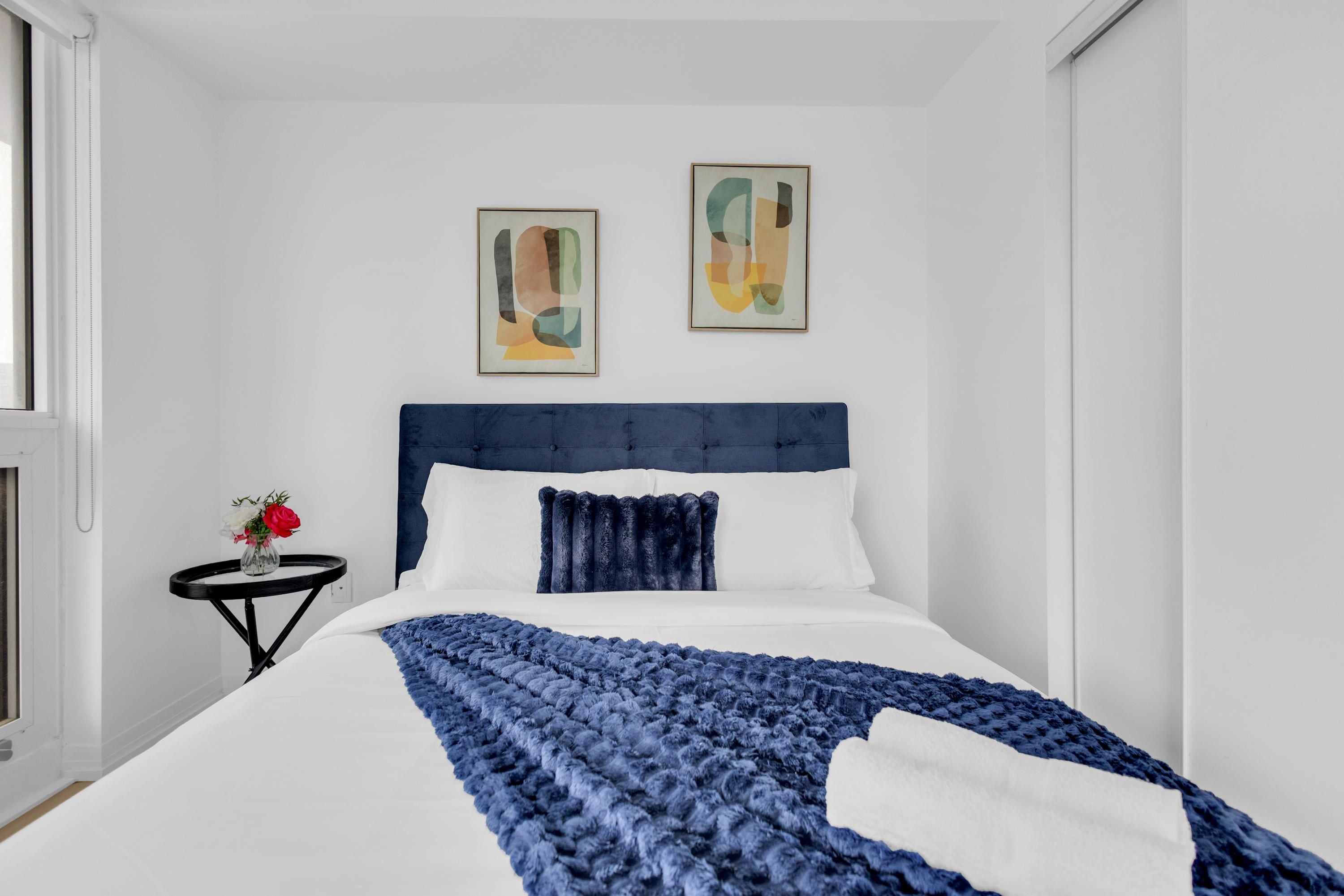 Un dormitorio moderno con una cama grande, una mesita de noche con flores y arte abstracto en la pared.