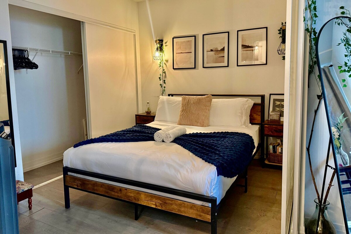 Een slaapkamer met een bed, nachtkastjes, een garderobe en lijstjes met foto’s aan de muur.