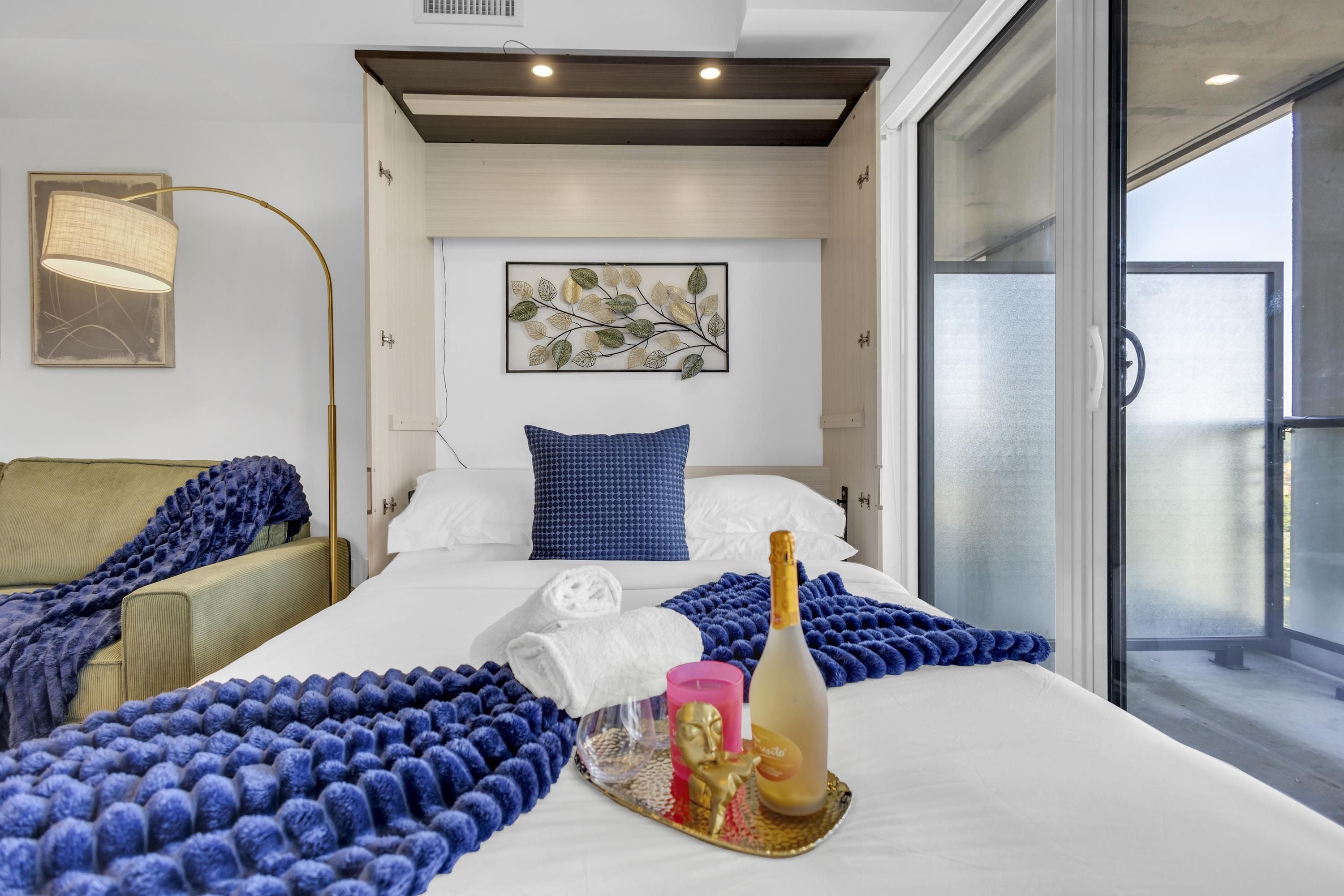 Habitación de hotel con una cama grande, una mesita de noche, una lámpara, un adorno en la pared y vistas al exterior.