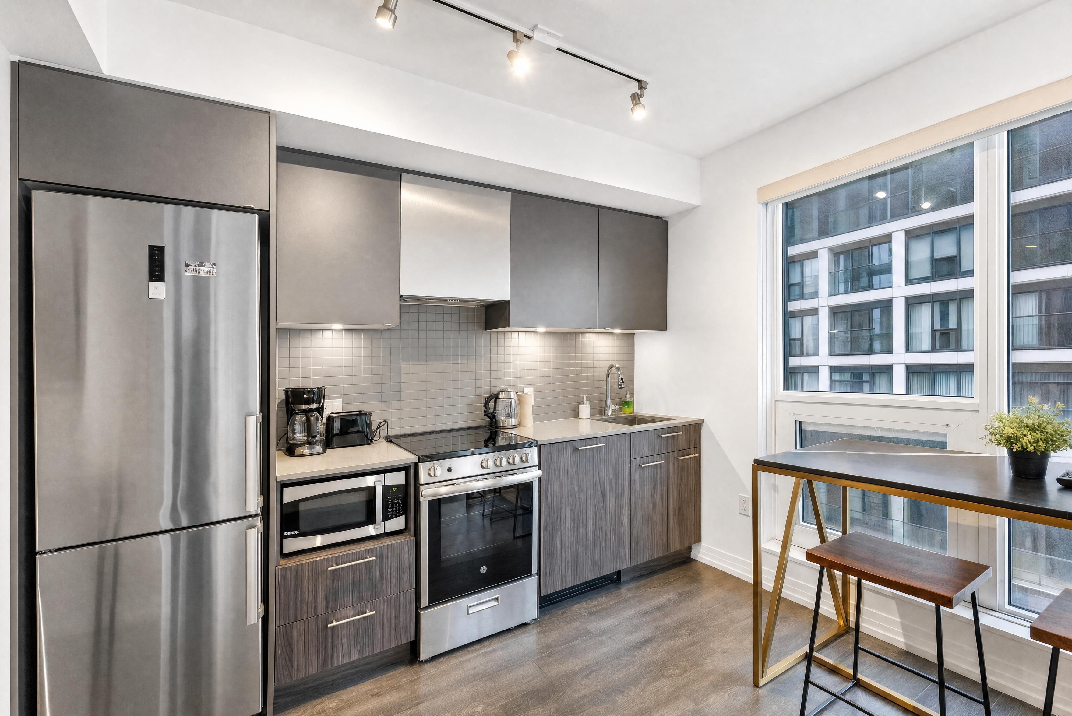 A modern kitchen with stainless steel appliances, a built-in oven, and a window overlooking a building.
