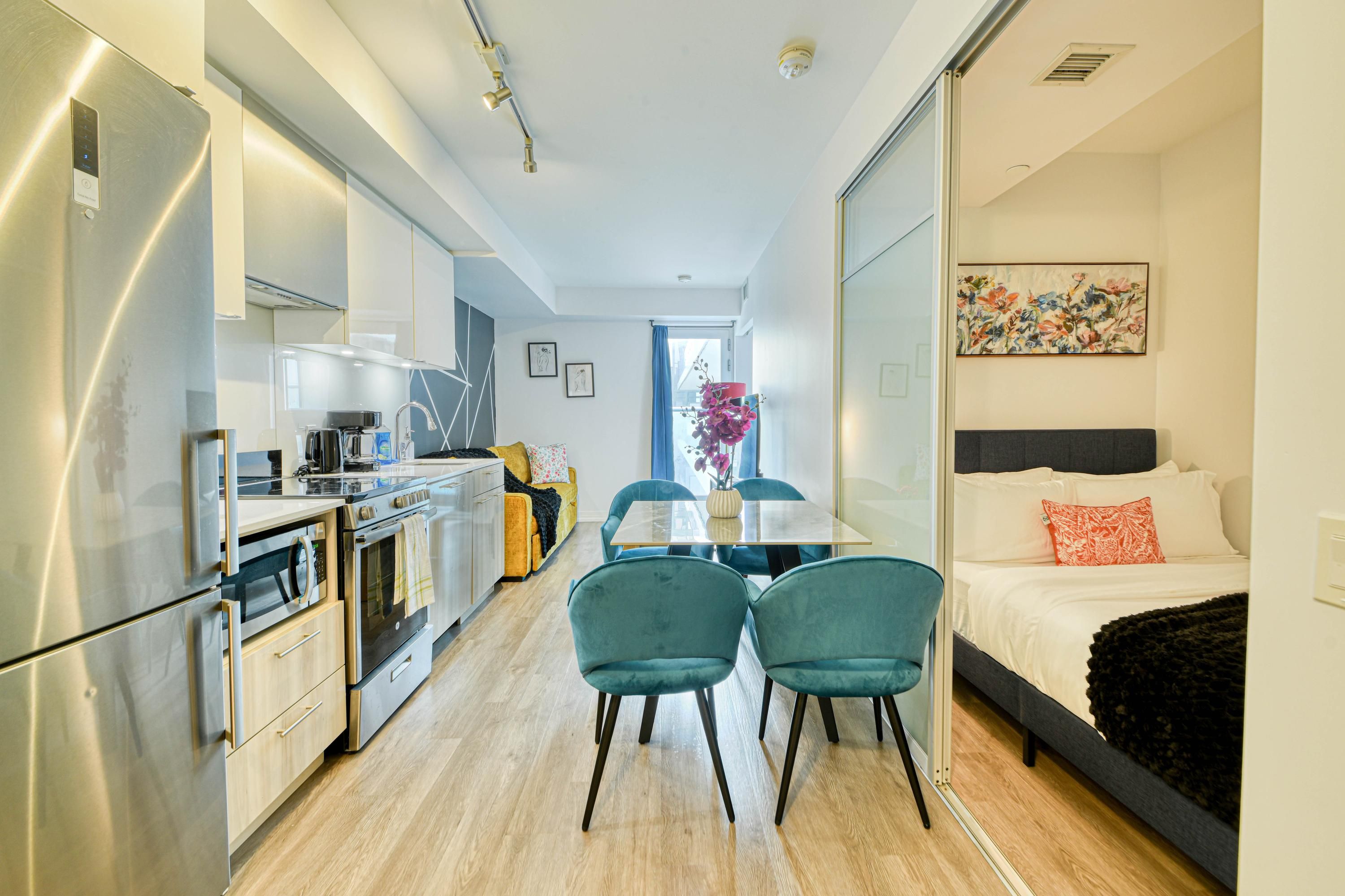 A compact hotel room with a kitchenette, a dining area, and a bed.