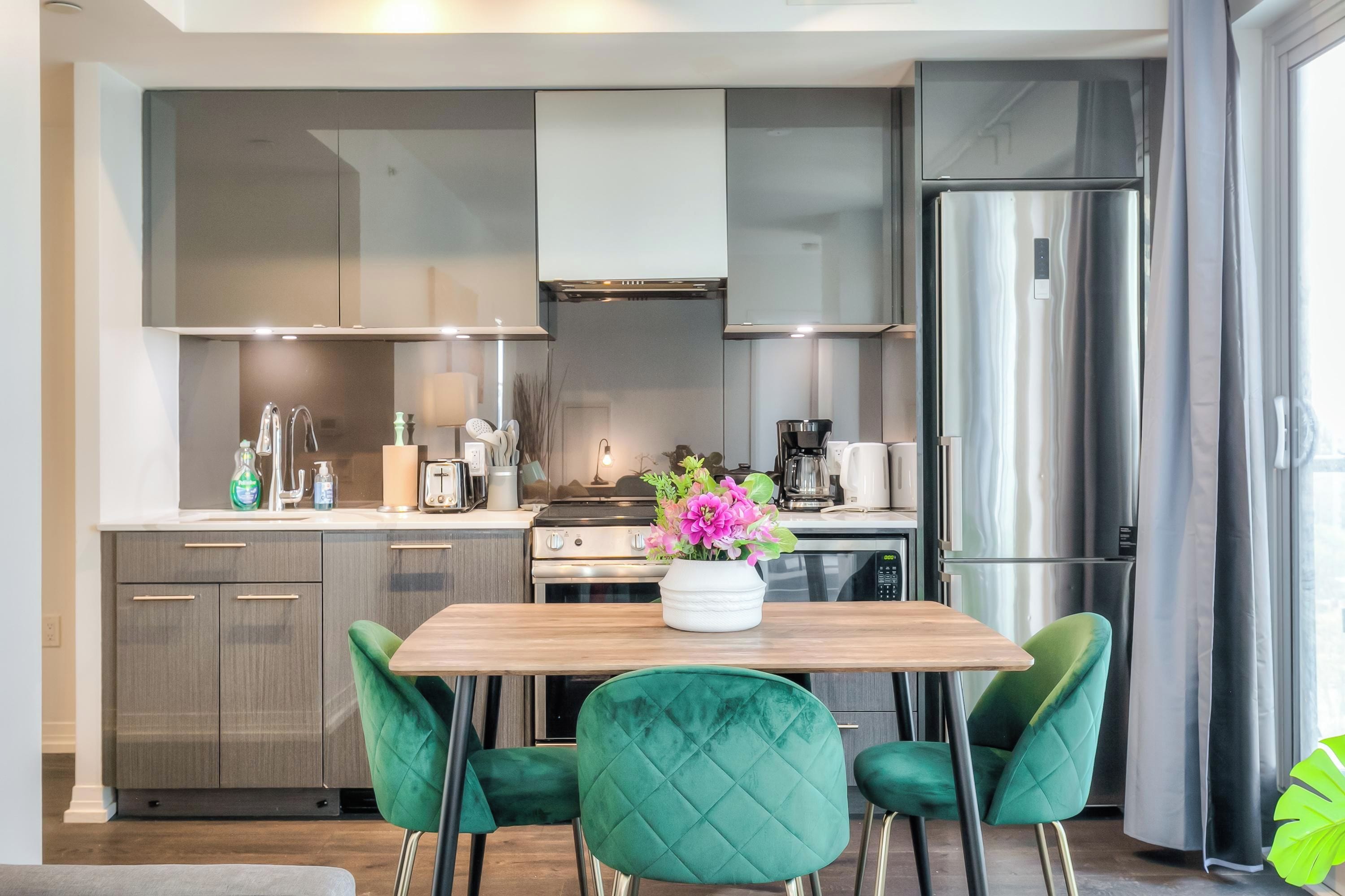 Una cocina moderna con una mesa de madera, sillas verdes y un refrigerador de acero inoxidable.