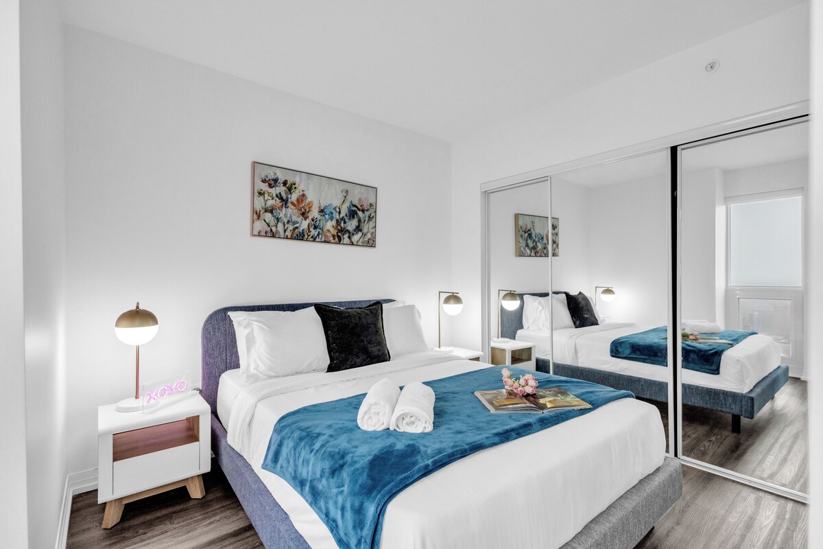 Een moderne hotelkamer met een groot bed, een nachtkastje met een lamp, een spiegel en een bloemwerk op de muur.