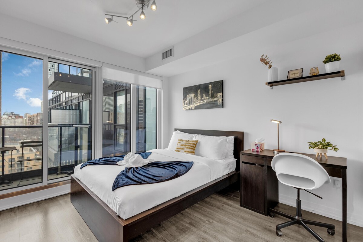 Een moderne hotelkamer met een groot bed, een bureau, een stoel, uitzicht op de stad en een schilderij aan de muur.